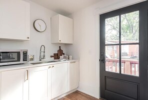 A kitchen with white cabinets, a microwave, a sink, and a clock on the wall.