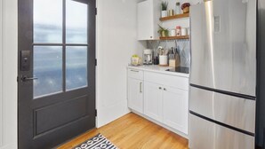 A compact kitchen with white cabinets, a stainless steel refrigerator, and a small countertop with various items.