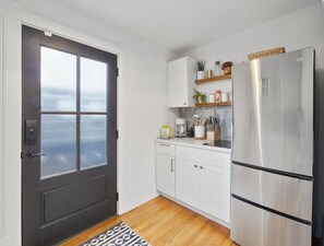 A compact kitchen with white cabinets, a stainless steel refrigerator, and a small countertop with various items.