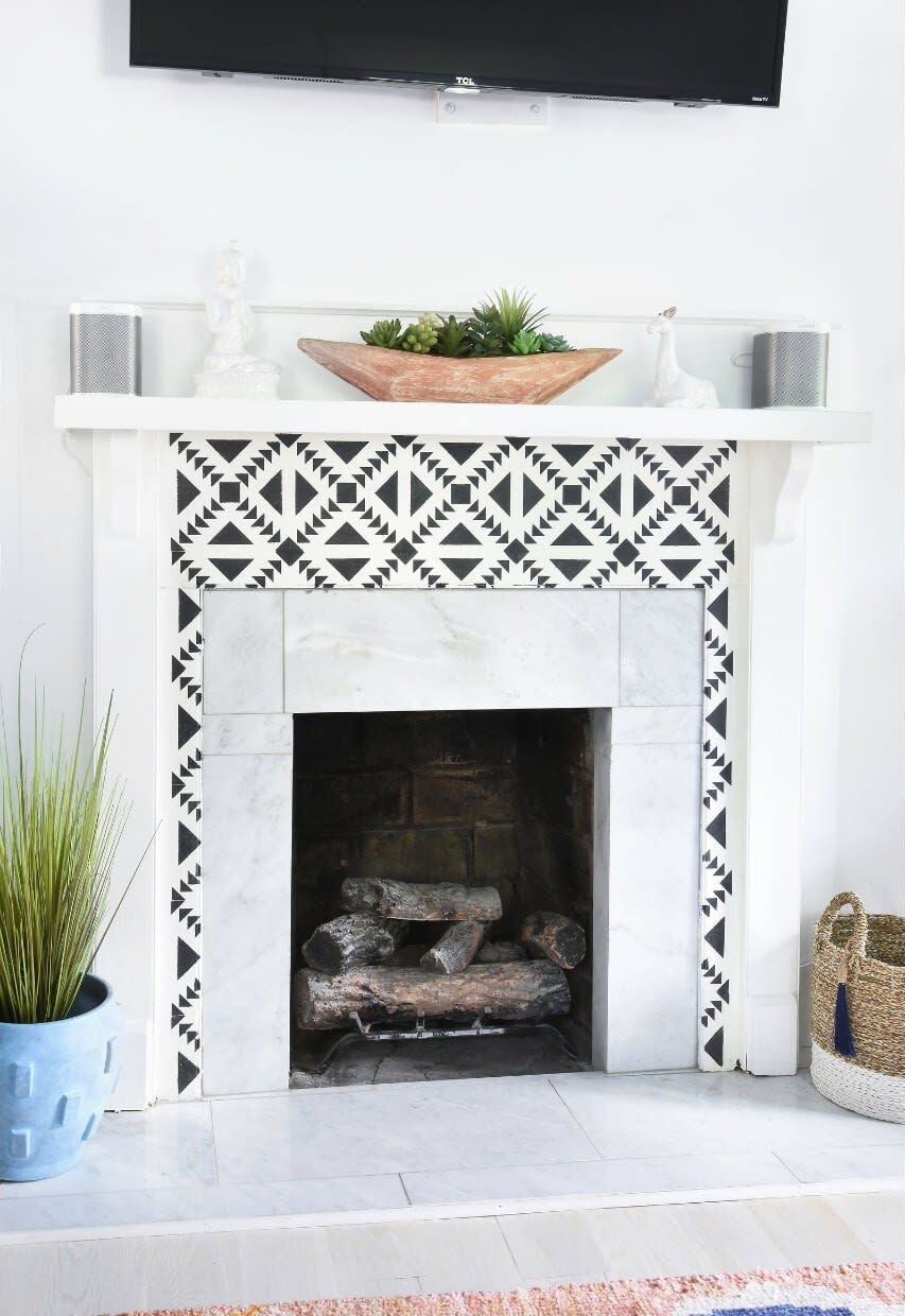 A fireplace with a geometric patterned surround, a mounted TV above it, and a potted plant to the left.