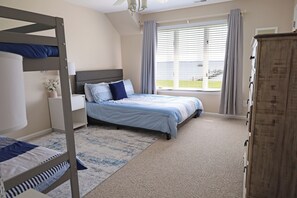 Une chambre avec des lits superposés, une grande fenêtre avec des rideaux et un sol recouvert de moquette.
