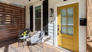A porch with a yellow door, a ceiling fan, and a chair with a vase of flowers. - Whiskey Neat (Atlanta)