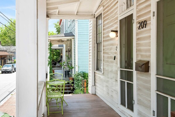 A porch with a green chair, a wooden deck, and a building with the number 209.