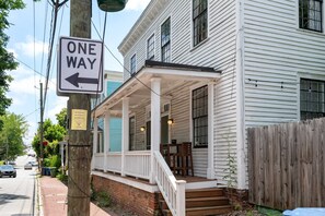 A white building with a porch, a one-way sign, and a wooden fence.
