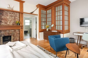 A room with a brick fireplace, wooden cabinets, a blue chair, a desk, and a television.