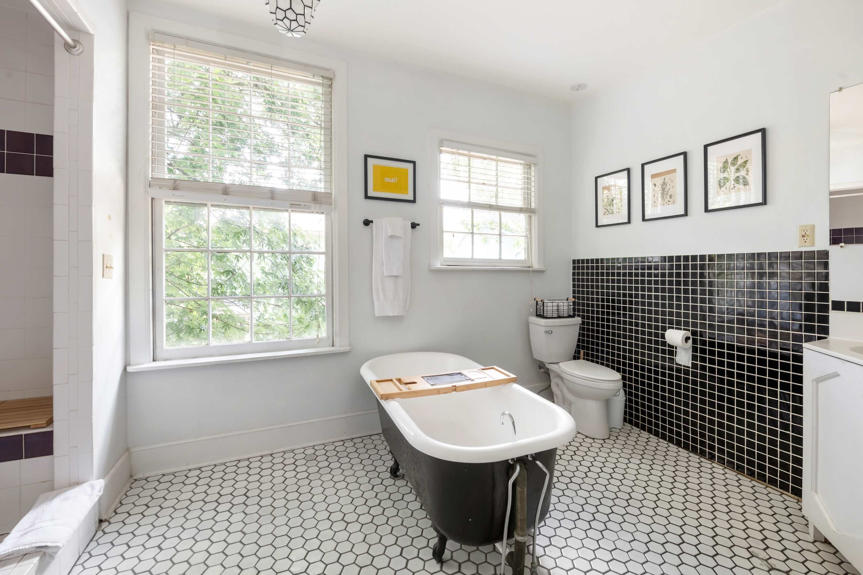 A bathroom with a black bathtub, white toilet, and black and white tiled floor.