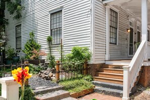 Una casa de madera blanca con porche, escalones y un jardín con plantas y flores.