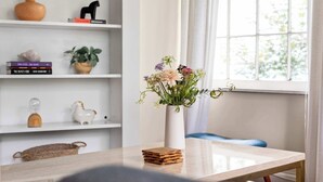 Una stanza con un tavolo bianco, un vaso con fiori e una libreria piena di libri e oggetti decorativi.