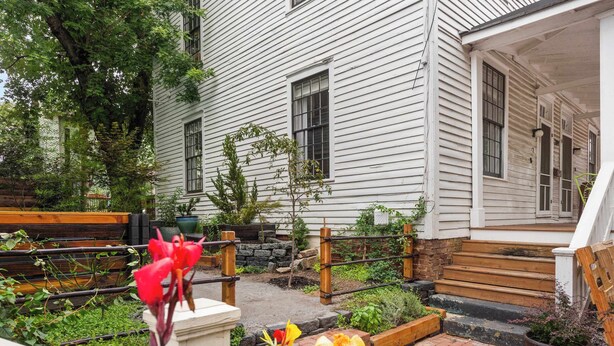 Una casa bianca in legno con un portico, delle scale e un giardino pieno di fiori e piante.