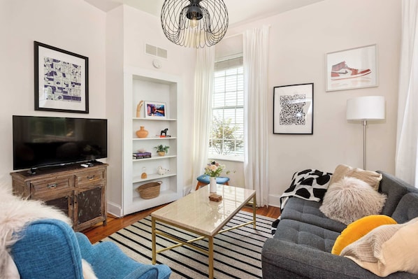 A modern living room with a flat-screen TV, a sofa, a coffee table, and a bookshelf.
