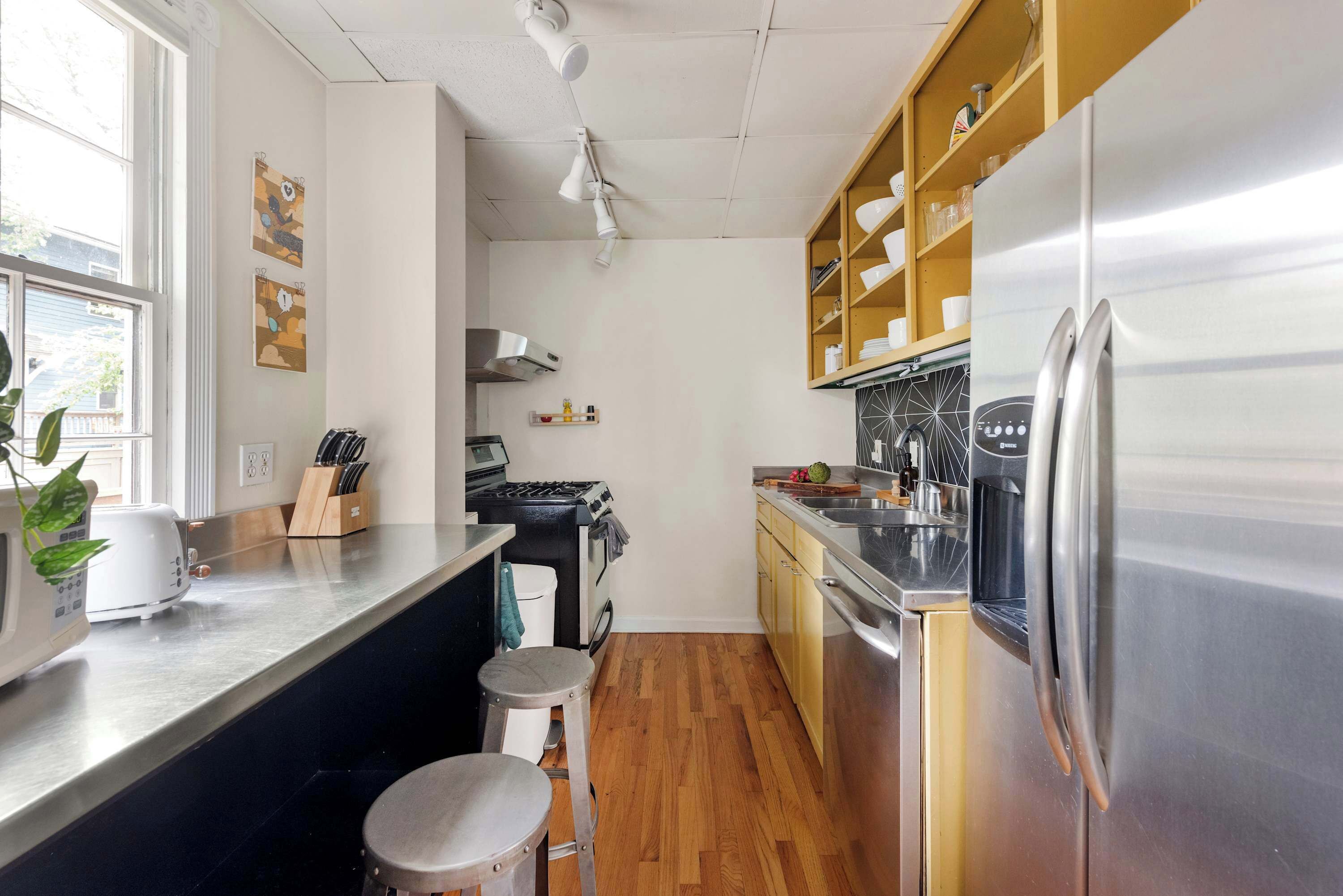 A modern kitchen with stainless steel appliances, wooden cabinets, and a window providing natural light.