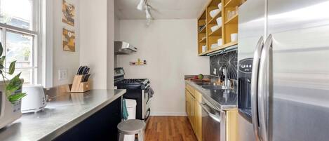 A modern kitchen with stainless steel appliances, wooden cabinets, and a window providing natural light.