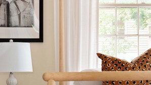 Una camera da letto con un letto con struttura in legno, biancheria da letto bianca, un cuscino decorato, una lampada da comodino e un quadro appeso al muro.