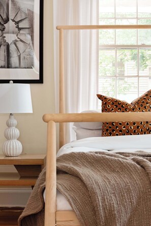 A bedroom with a wooden bed frame, white bedding, a patterned pillow, a bedside lamp, and a framed artwork on the wall. - Down the Rabbit Hole (Atlanta)