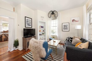 A modern living room with a TV, sofa, and coffee table. There is a bookshelf and a window with curtains.