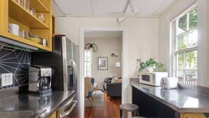 Una cucina moderna con macchina da caffè, forno a microonde e tostapane. Il pavimento è in legno, c'è un'area pranzo con un tappeto a righe e una vista all'esterno attraverso una finestra.