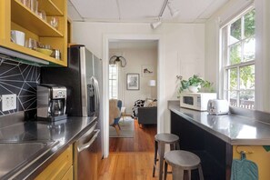 A modern kitchen with a coffee maker, microwave, and toaster. There is a wooden floor, a dining area with a striped rug, and a view of the outdoors through a window. - Down the Rabbit Hole (Atlanta)