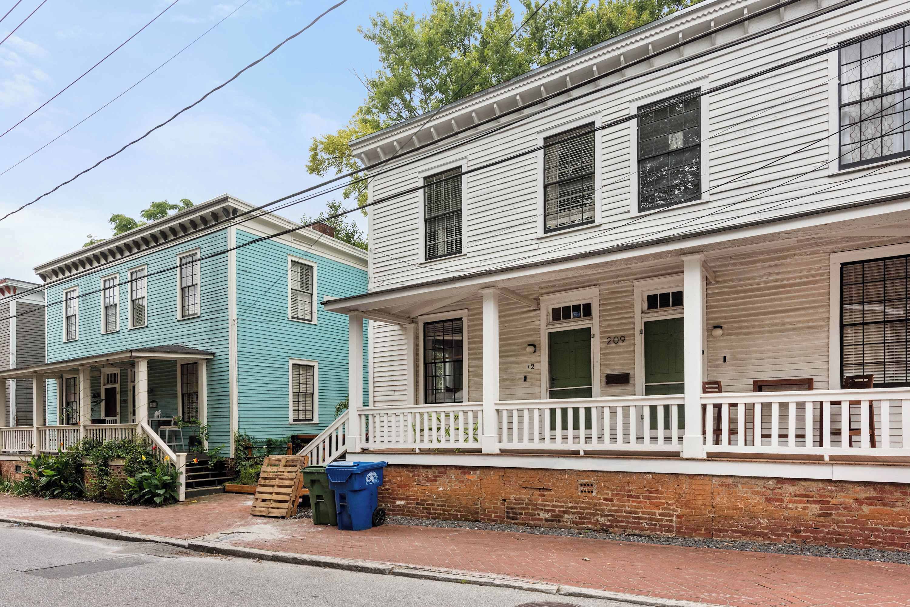 A row of two-story houses with white and teal exteriors, a brick foundation, and a front porch with a white railing.
