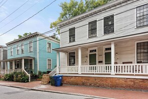 A row of two-story houses with white and teal exteriors, a brick foundation, and a front porch with a white railing.