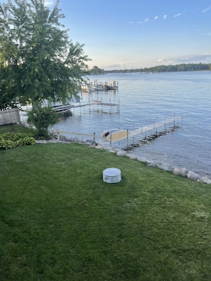 A grassy area with a dock extending into a calm lake, surrounded by trees and a clear sky.