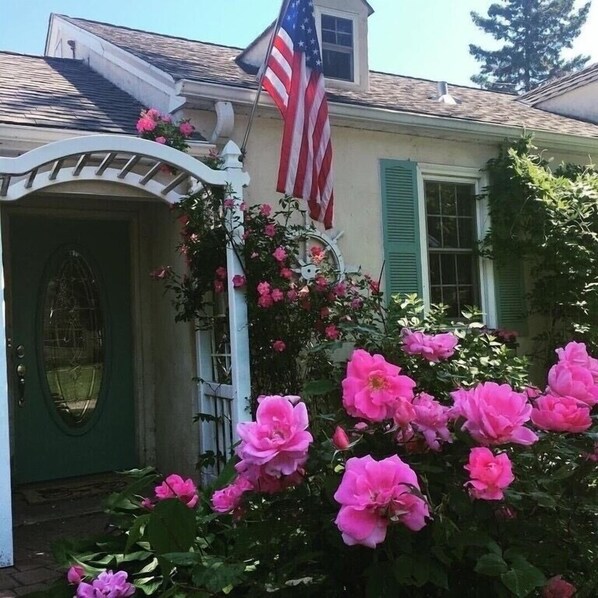 A house with a green door, a white porch, and pink flowers.