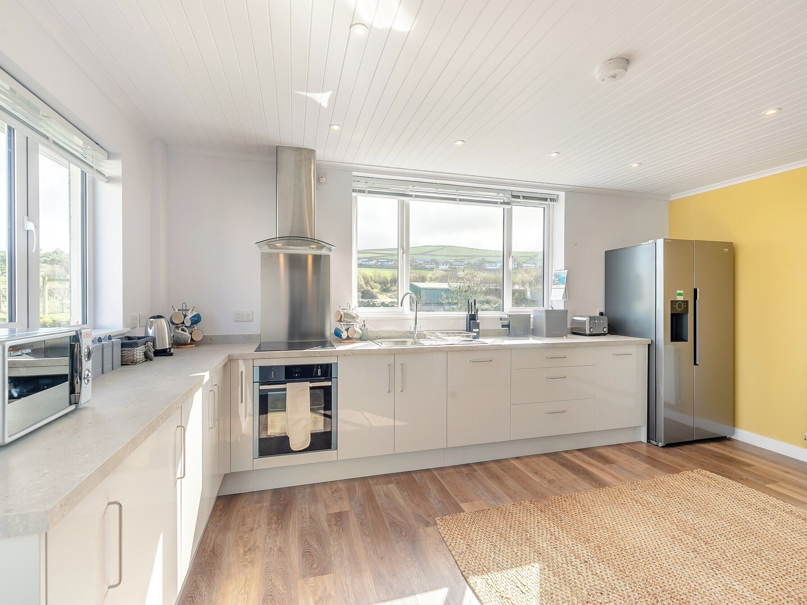 Une cuisine moderne dotée d’une grande fenêtre, d’appareils électroménagers en acier inoxydable et d’un plancher en bois.