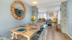 Un coin repas avec une table en bois dressée pour quatre personnes, un miroir avec un cadre en bois et un vase rempli de fleurs jaunes.