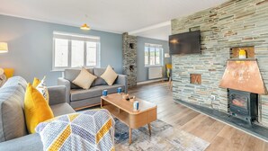 Un salon avec une cheminée en pierre, un canapé gris et un téléviseur fixé au mur.