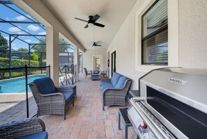An outdoor patio with wicker furniture, a grill, and a pool in the background. - 6BR Family Friendly Resort Pool Home Near Disney (Davenport)