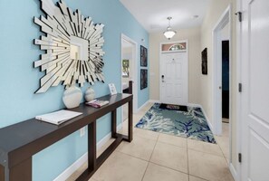 A hallway with a dark wooden console table, a decorative wall piece, and a patterned rug leading to a white door. - 6BR Family Friendly Resort Pool Home Near Disney (Davenport)