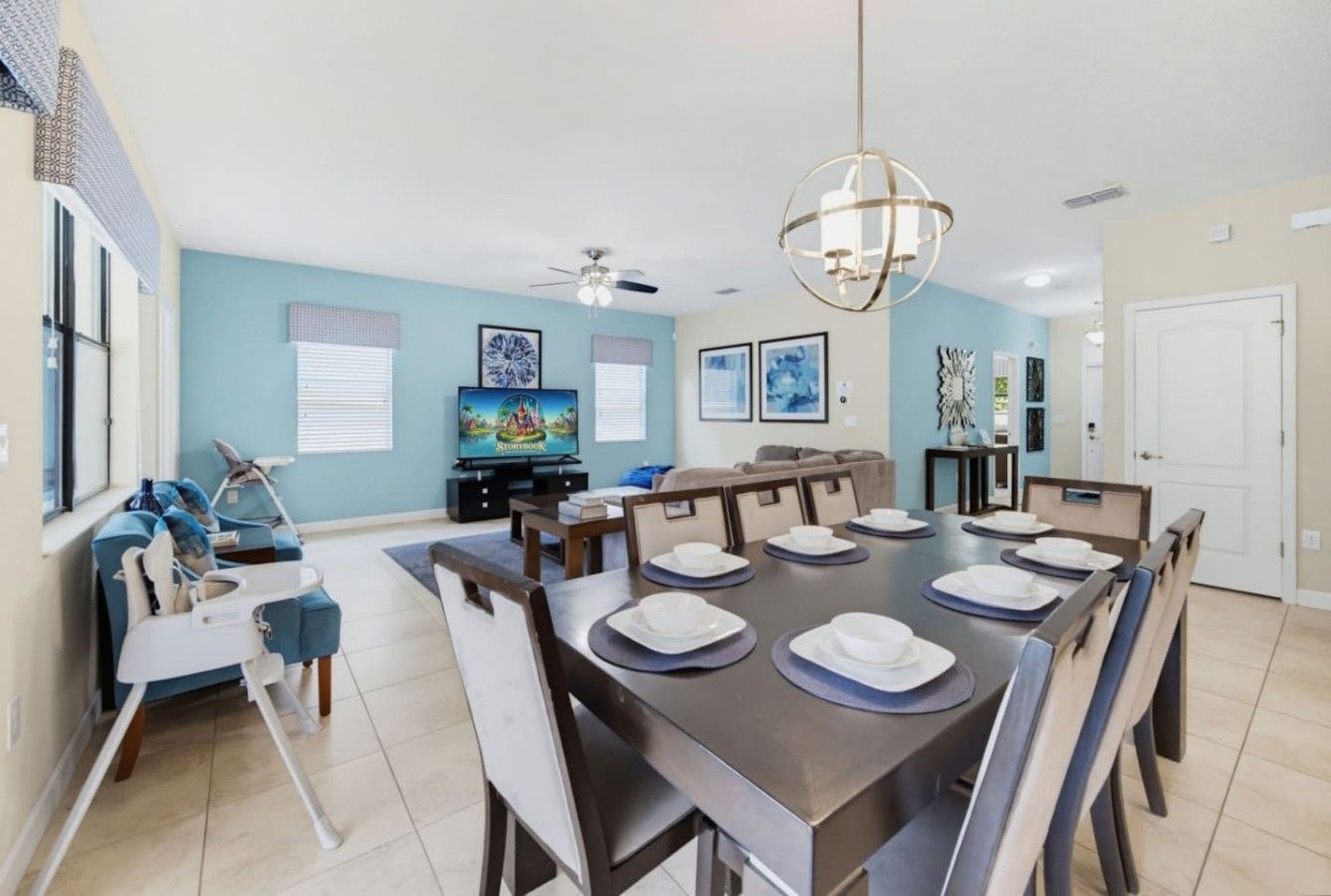A dining area with a large table set for six, a high ceiling fan, and a television on a stand.