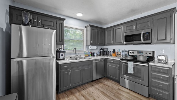 Una cocina moderna con electrodomésticos de acero inoxidable, armarios grises y suelo de madera.