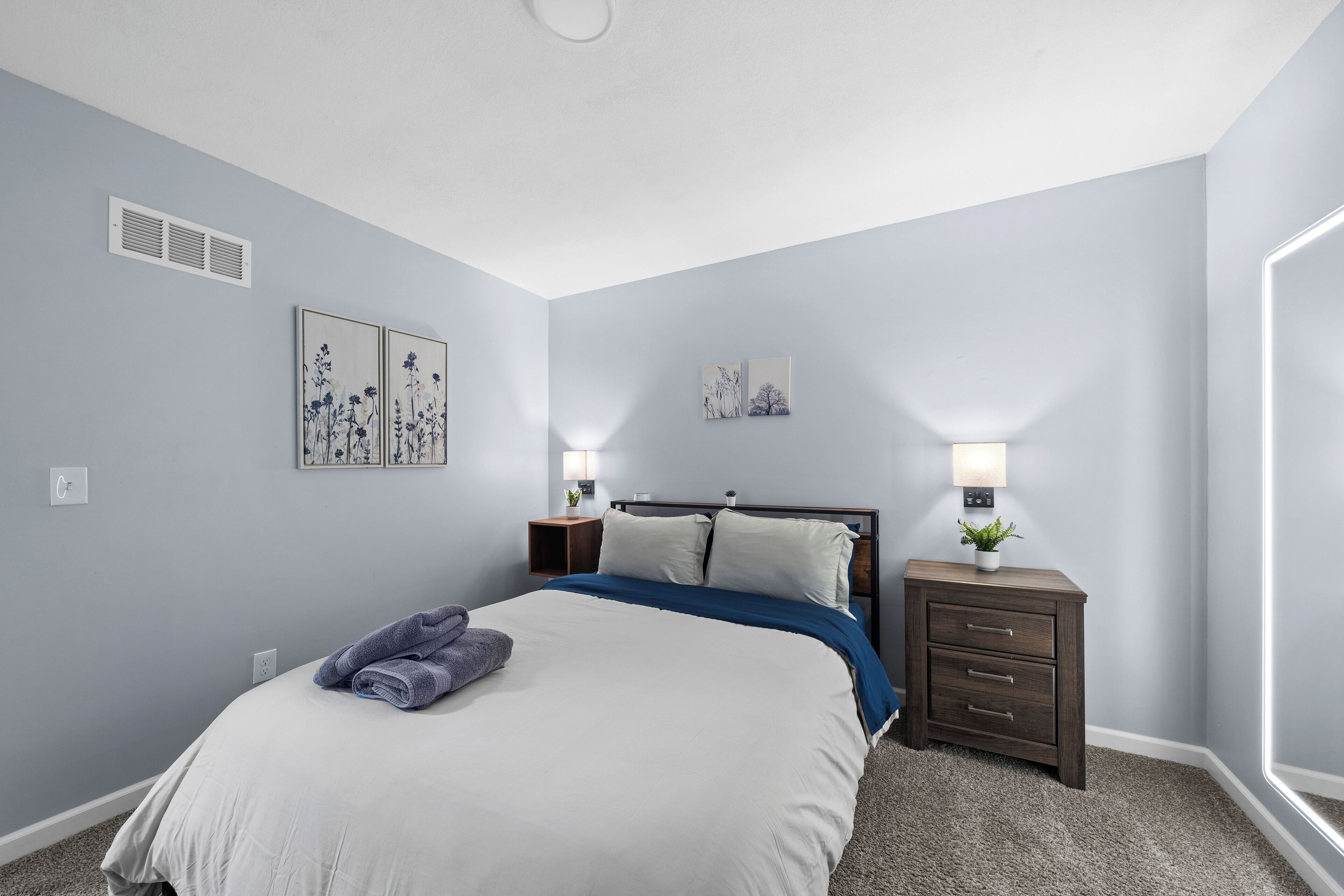 A bedroom with a bed, nightstands, wall art, and a window.
