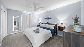 Un dormitorio con cama, mesitas de noche, escritorio, ventilador de techo y vistas al exterior.