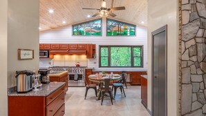 A kitchen with wooden cabinets, a dining area, and a stone accent wall. - Private Mountain Home, 2miles To Ski, Hot Tub, Views, Fireplace, & Pet Friendly! (Beech Mountain)