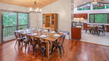 Een ruime eetruimte met een houten tafel voor zes personen, omringd door stoelen. In de achtergrond is een grote houten kast zichtbaar, en de kamer heeft grote ramen met uitzicht op het omliggende landschap.