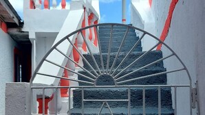 Um portão de metal com design em forma de sol que dá acesso a uma escadaria com corrimão vermelho e branco.