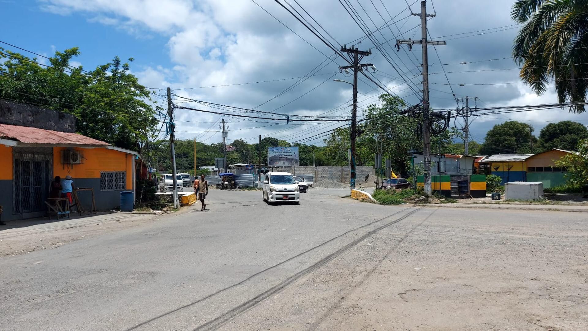 A street with buildings, a white car, and utility poles.