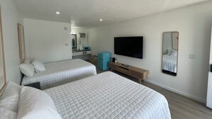 A hotel room with two beds, a TV, a mirror, and a kitchenette. - Double Queen Room Sum (Lake City)