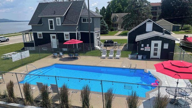 A swimming pool with a fenced deck, surrounded by a house and a small building with a lifeguard sign. - Double Queen Room Sum (Lake City)