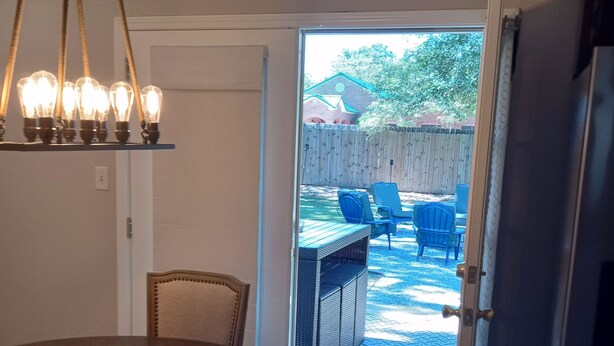 A dining area with a round table and chairs, a kitchen with a refrigerator, and an open door leading to an outdoor patio with chairs and a table. - Charming Home Comfy Beds Private Backyard with Fire Pit  (Hattiesburg)