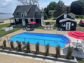 A swimming pool with a fenced deck, surrounded by a house and a small building with a lifeguard station. - Single Queen Room w/ Sleeper Sofa (main level) (Lake City)