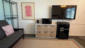 A living room with a grey sofa, a flat-screen TV, a microwave, and storage bins. - Single Queen Room w/ Sleeper Sofa (main level) (Lake City)