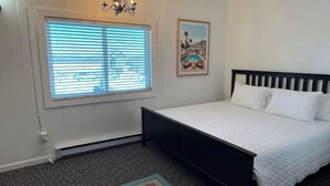 A bedroom with a bed, a window with blinds, a wall-mounted picture, and a carpeted floor. - Single Queen Room w/ Sleeper Sofa (main level) (Lake City)
