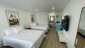Een hotelkamer met twee bedden, een kleine kitchenette, een televisie en een badkamer met een spiegel.