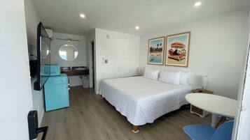 Una habitación de hotel con cama, escritorio, silla, kitchenette pequeña y baño.