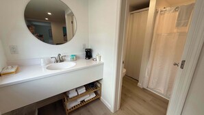 A modern bathroom with a white sink, a round mirror, and a shower area.