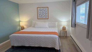 A neatly made bed with a white quilt, two bedside lamps, and a framed artwork above it.
