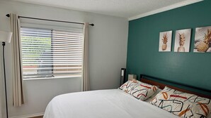 Une chambre à coucher avec un lit, une fenêtre avec des stores, une lampe sur pied et trois tableaux accrochés au mur.