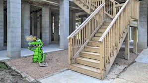 Un sitio de construcción con una escalera de madera y un cartel de bienvenida con un cocodrilo de dibujos animados.